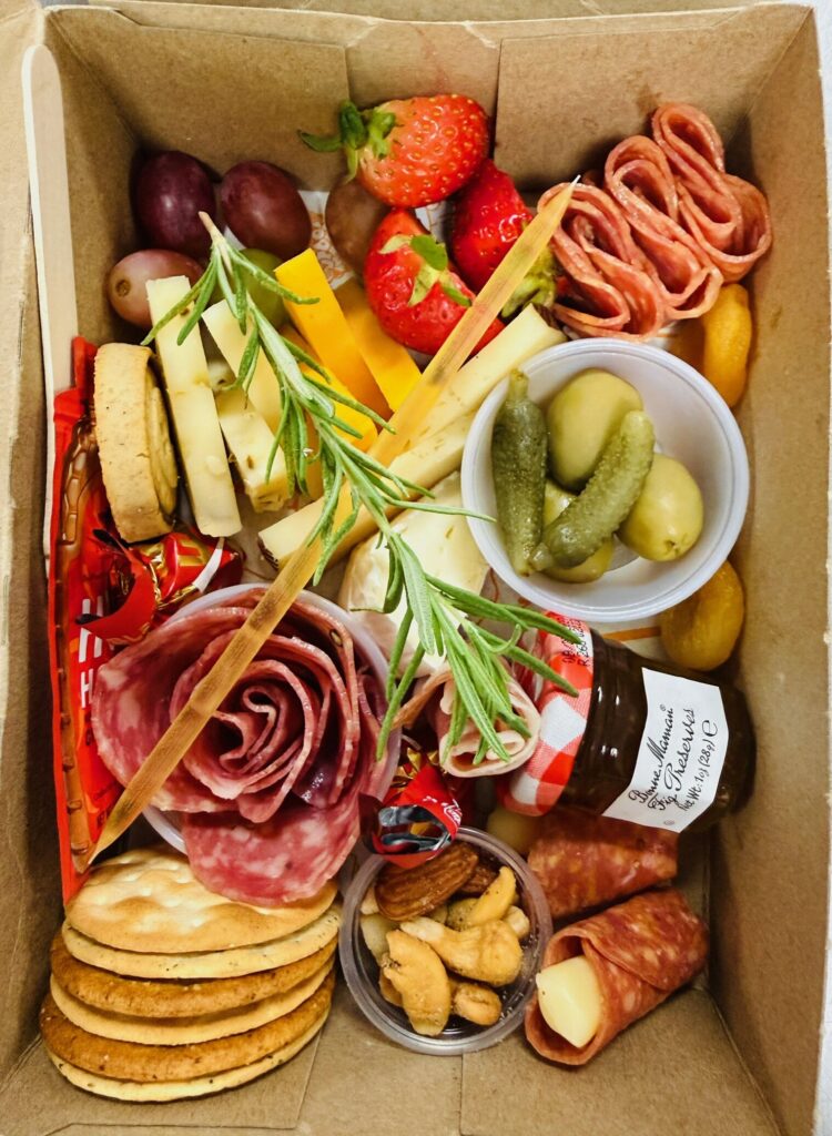 Open elevated charcuterie box with salami rose, cheeses, fruit and crackers