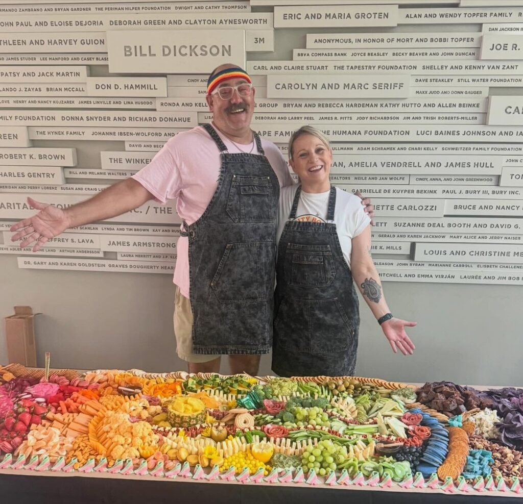 Corey Riser and Brie Grant with a rainbow grazing table at ZACH Theatre