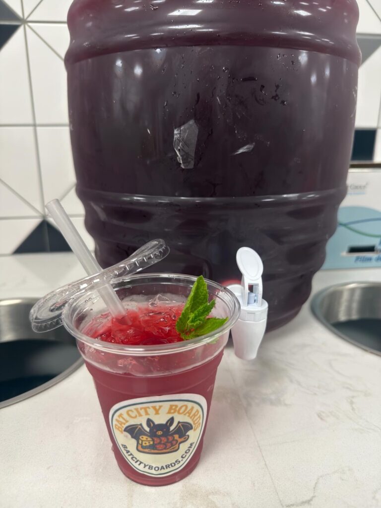 Hibiscus agua fresca in a dispenser with a Bat City Boards cup