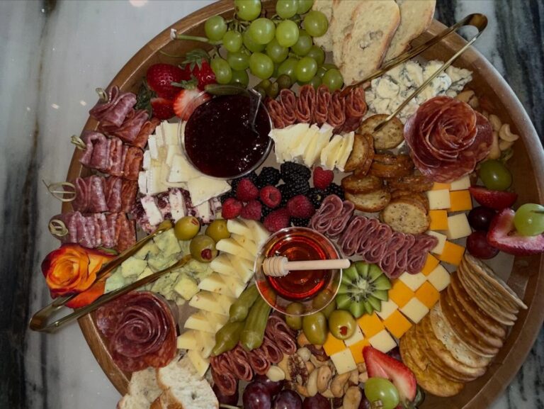 Round board with salami rose, berries, olives and jam on marble