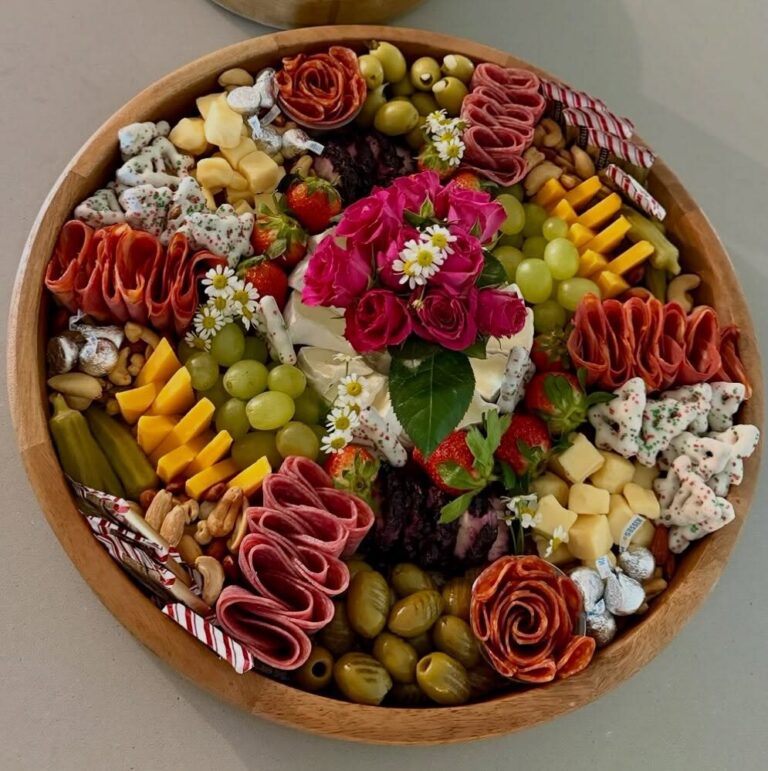 Round holiday charcuterie board with flowers, salami roses, grapes and cheeses